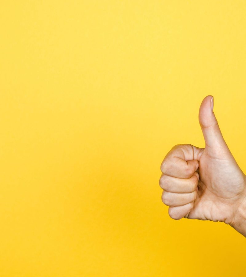 closeup of thumbs up symbol on yellow background.
